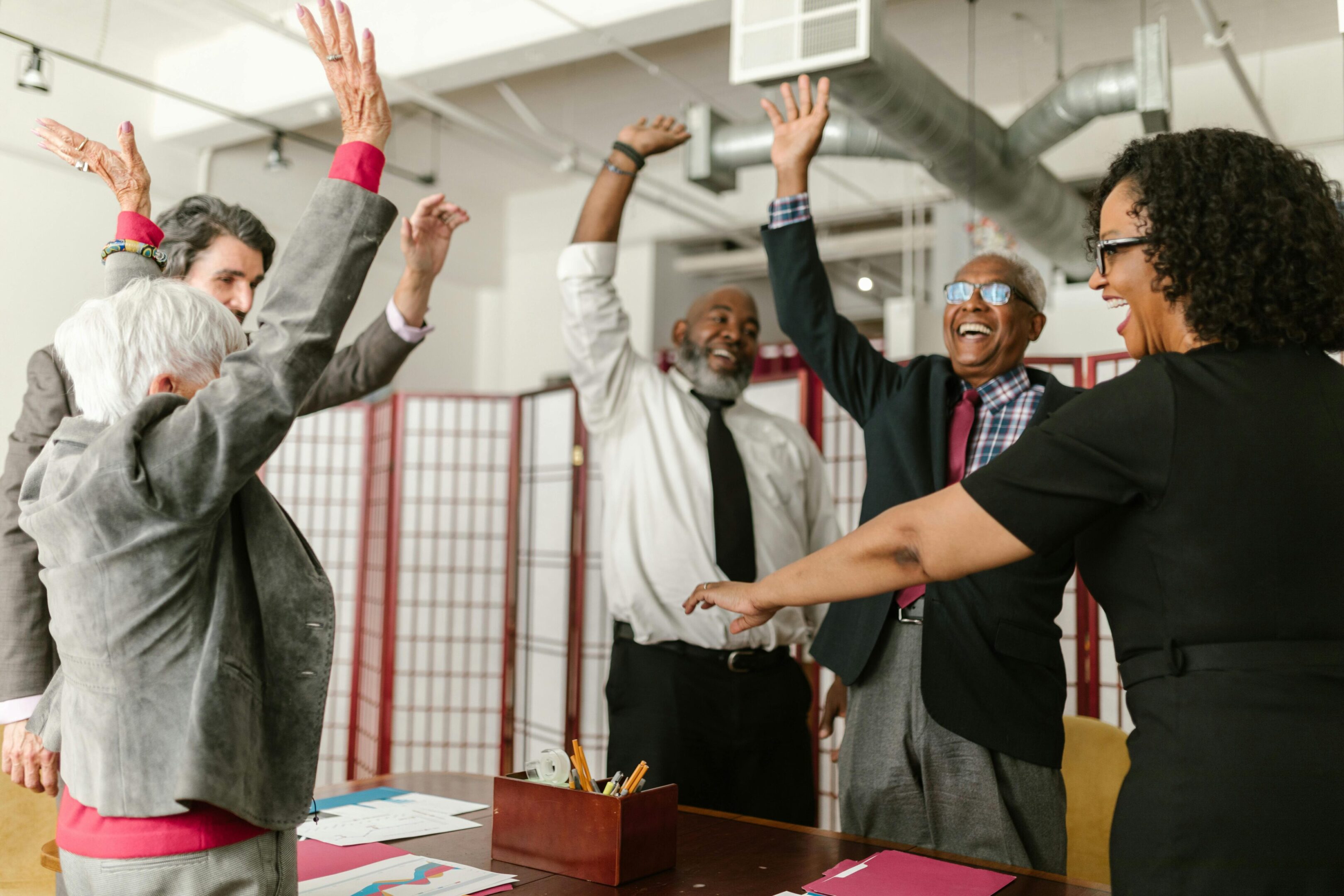 A group of people standing around a table with their hands raised.